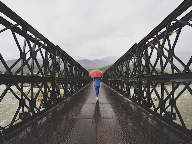 写真 雨季の川の橋の上で傘をかぶった人の後ろの景色