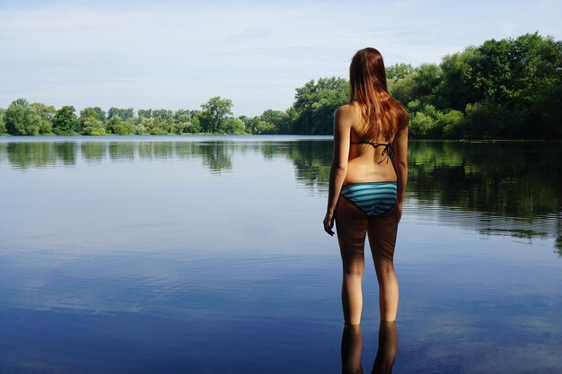 写真 湖に立っているビキニを着た感性的な女性の後ろの景色