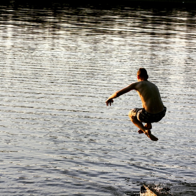 写真 湖を飛び越えるシャツのない男の後ろの景色