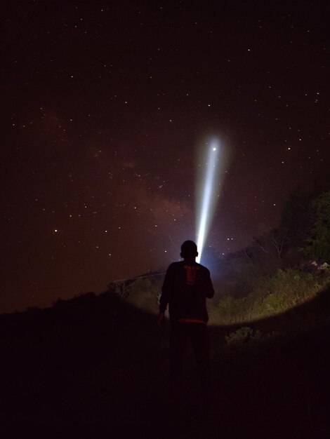 写真 夜に星を見ている手電筒を用いたシルエットハイカーの後ろの景色