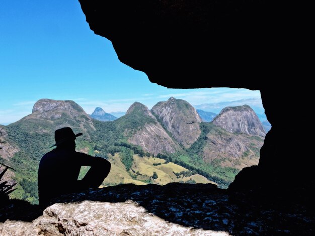 写真 空の向こうの岩の上に座っているシルエットの男の後ろの景色