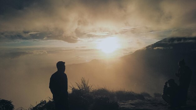 写真 空の向こうの山の上に立っているシルエットの男の後ろの景色