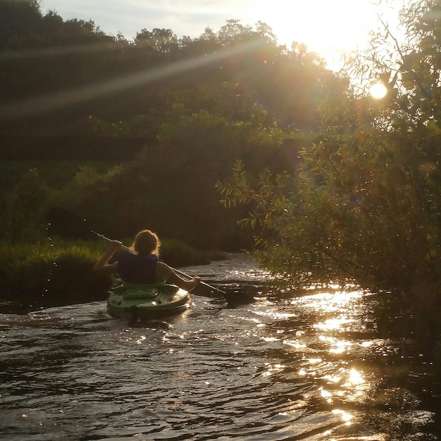 Фото Задний вид женщины, катающейся на лодке на реке против дерева