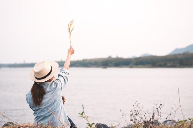 写真 明るい空に照らされて湖のそばで植物を抱いている女性の後ろの景色