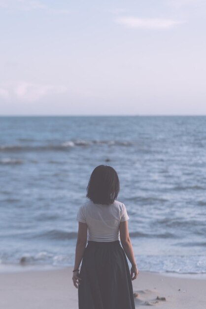 写真 空を背景に海を見ている女性の後ろの景色