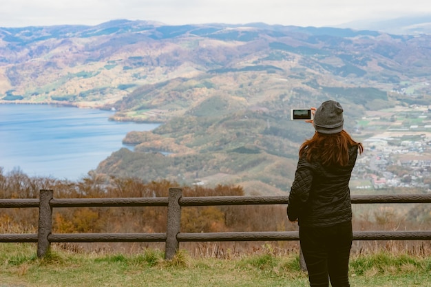 写真 山の反対側のレールに立って写真を撮っている女性の後ろの景色
