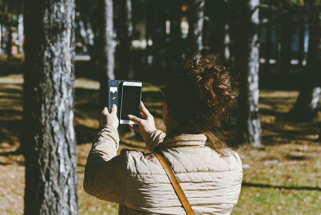 사진 숲에서 휴대전화로 사진을 찍는 여성의 뒷면