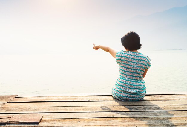 写真 堤防に座っている女性が海を指している後ろの景色