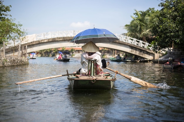 Задний вид женщины, гребающей на лодке в реке напротив моста