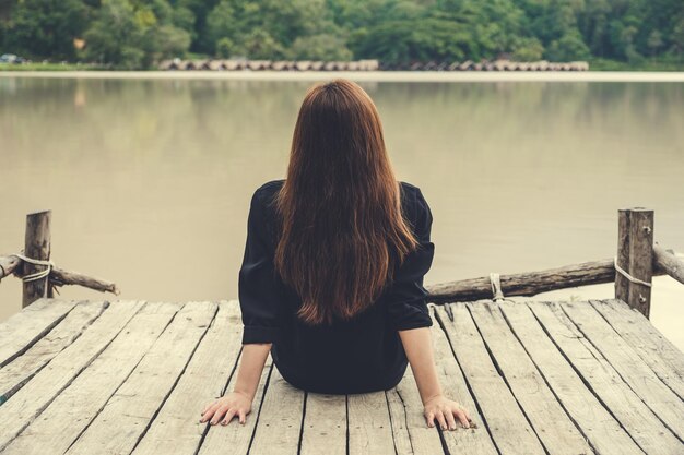 写真 湖の埠頭に座っている女性の後ろの景色