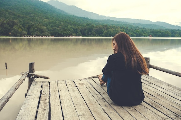 写真 湖の上の埠頭に座っている女性の後ろの景色