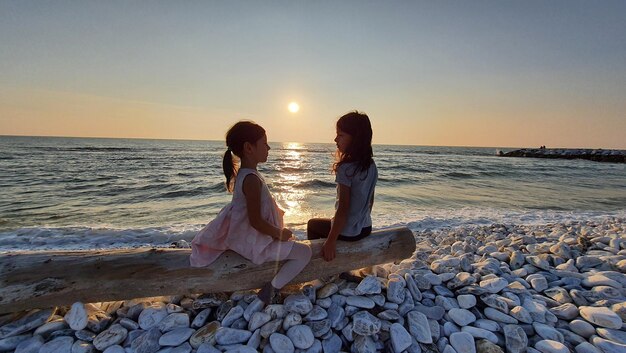 写真 夕暮れの空に照らしてビーチの岩の上に座っている女性の後ろの景色