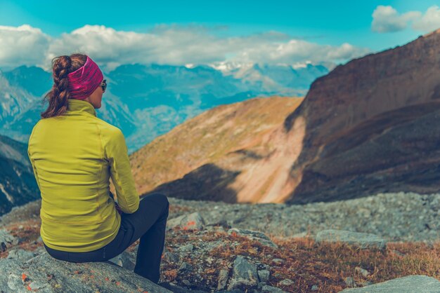 写真 岩の上に座って山を見ている女性の後ろの景色