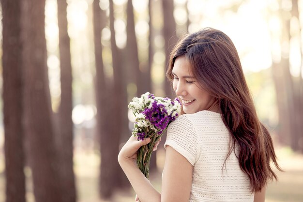 写真 森で花をんで笑顔を浮かべている女性の後ろの景色