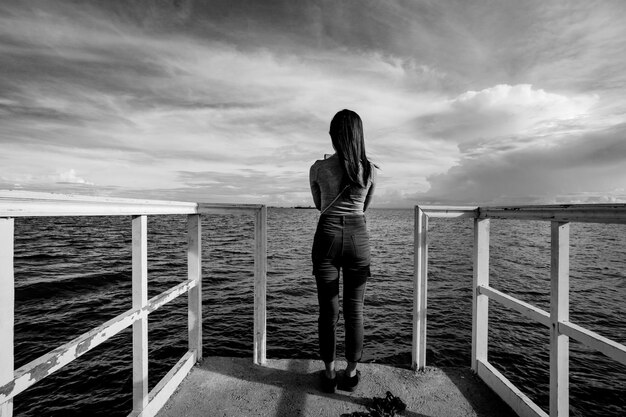 사진 바다 에 맞서 레일 을 고 서 있는 여자 의 뒷면