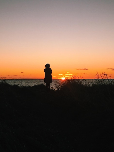 사진 해가 지는 동안 하늘을 배경으로 해변에 서 있는 여자 의 뒷면