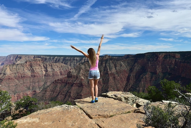 写真 空に向かって崖の上に立っている女性の後ろの景色