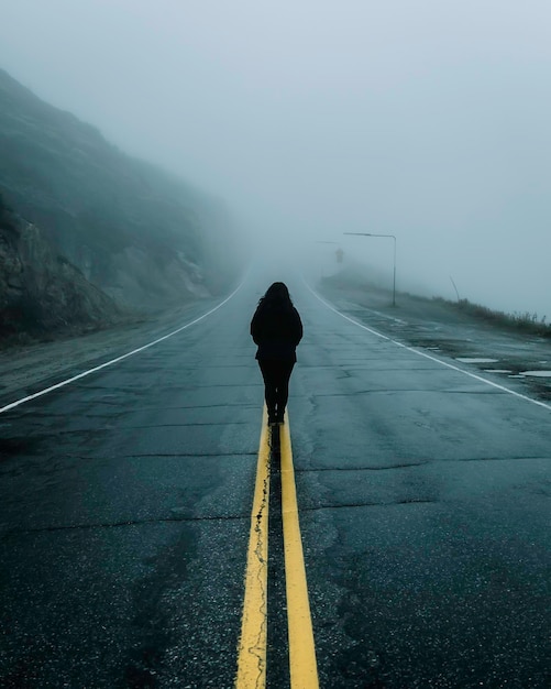 写真 霧の天候で道路に立っている女性の後ろの景色