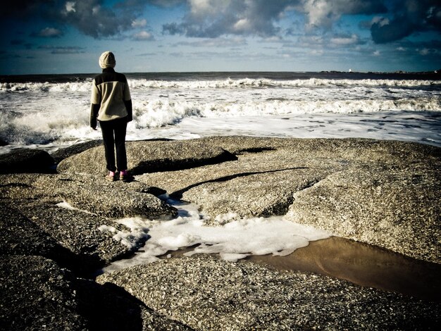 写真 海の向こうの岩の上に立っている女性の後ろの景色