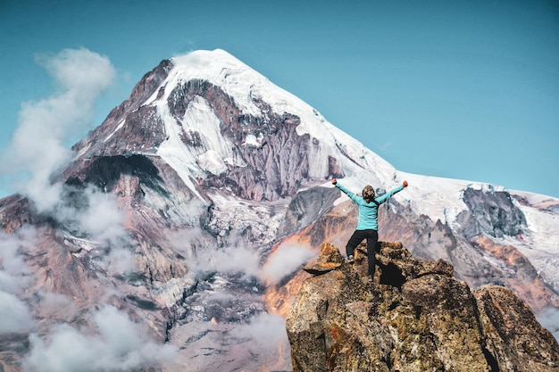 Фото Задний вид женщины, стоящей на скале с вытянутыми руками на гору и небо