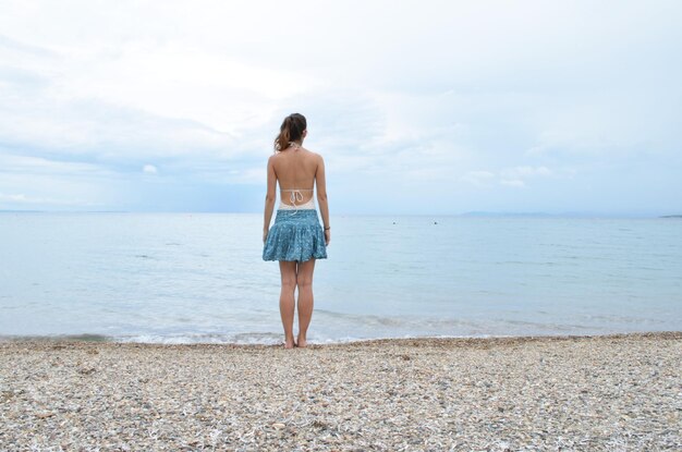写真 空の向こうのビーチで岸に立っている女性の後ろの景色