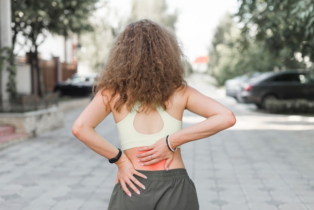 写真 腰痛を持つ通りに立っている女性のリアビュー