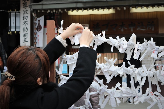 写真 寺院 で 紙 を 縛っ て いる 女性 の 後ろ の 景色