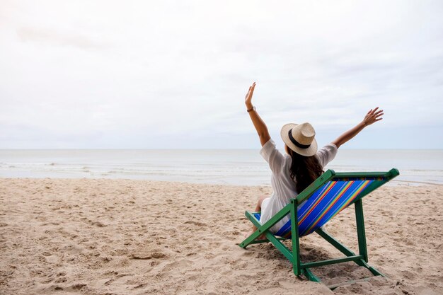 写真 浜辺のデッキチェアに座っている腕を伸ばした女性の後ろの景色