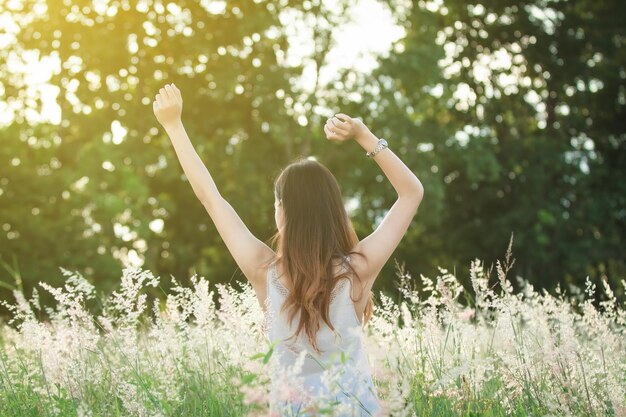 写真 畑の植物の真ん中に立っている腕を上げた女性の後ろの景色