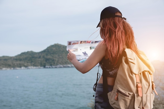 写真 空の反対側に海に立っている間バックパックを持った女性が地図を見ている後ろの景色