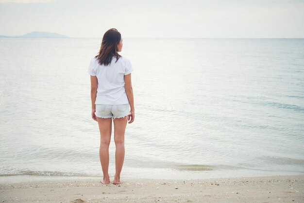 写真 浜辺に立っている若い女性の後ろの景色