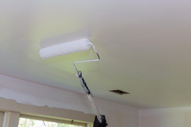 Rear view of painter paints the ceiling with a roller in\
room