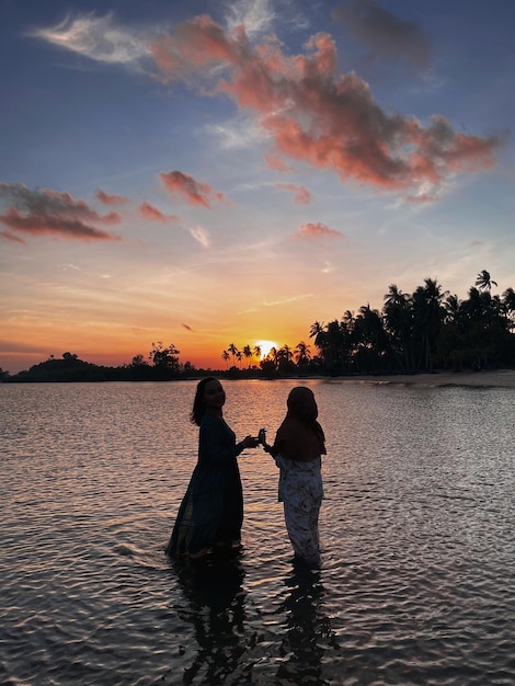 Rear view of people on lake against sky during sunset