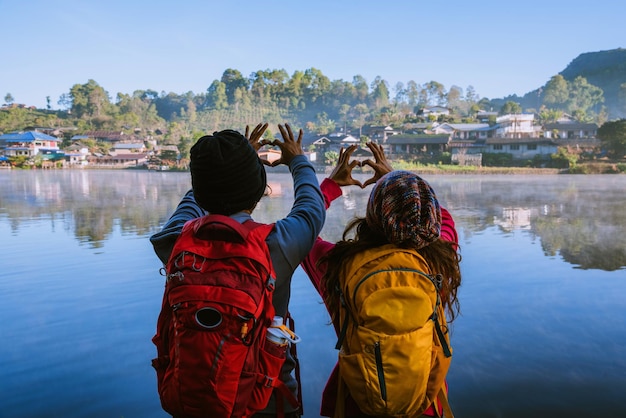 Foto vista posteriore di persone che fanno la forma di un cuore con le mani mentre stanno accanto al lago contro il cielo