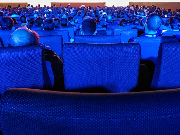 Photo rear view of people sitting on chairs at auditorium