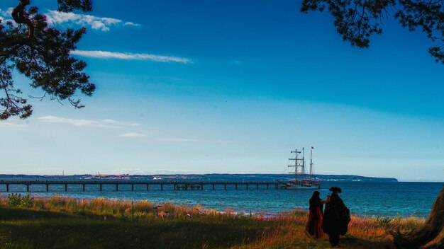 Rear view of people sitting on land by sea against sky