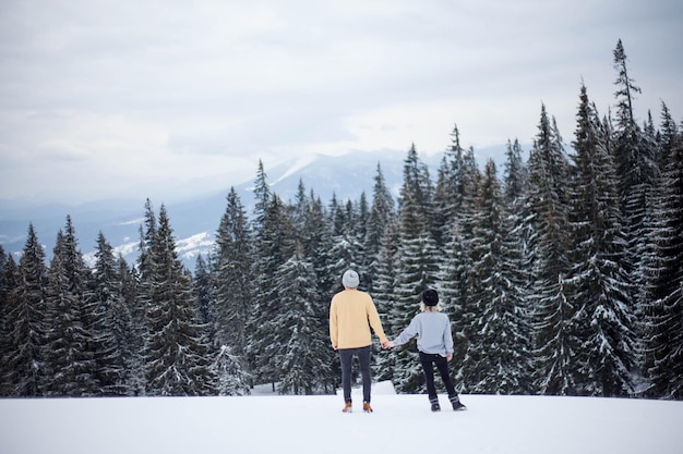 Rear view of people standing on snow covered landscape against trees