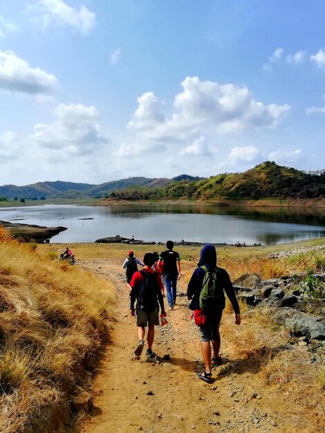 Rear view of people walking on footpath by lake