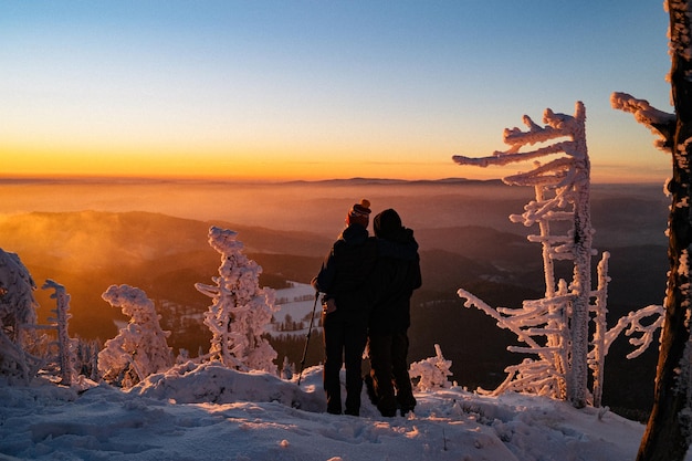 Rear view of people walking on snow covered landscape during sunset