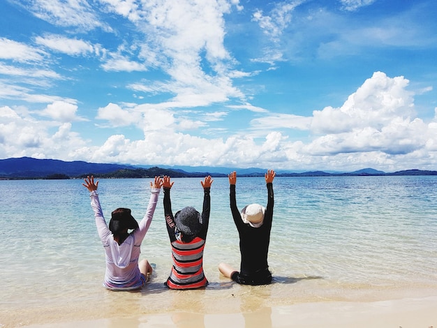 Rear view of people with arms raised sitting at beach against sky