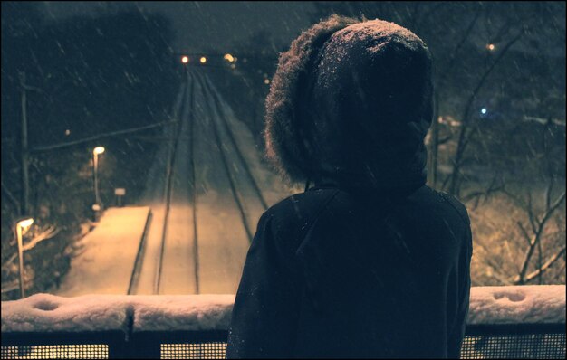 Photo rear view of person standing on footbridge over snow covered railroad tracks at night