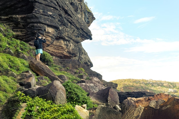 Rear View of Person Standing on Rock Tacking Picture whit His Smartphone to a Seaside Landscape