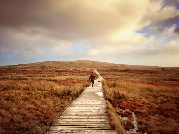 Photo rear view of person walking on boardwalk leading towards black mountain