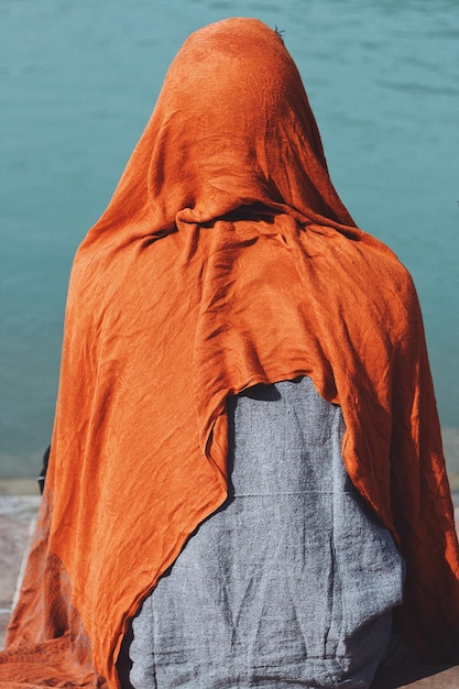 Foto vista posteriore di una persona con una sciarpa seduta sulla riva del fiume