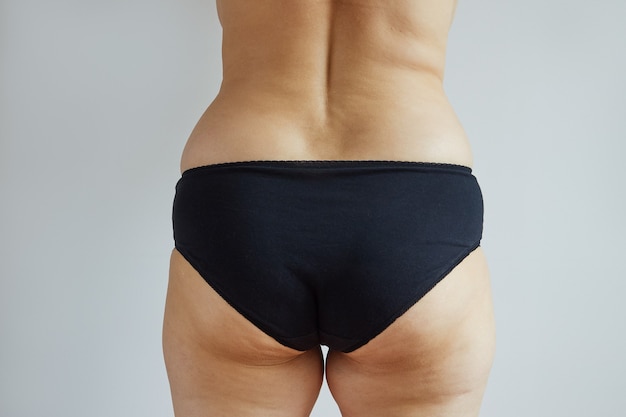 Rear view of a plump woman in black panties studio photo on gray background