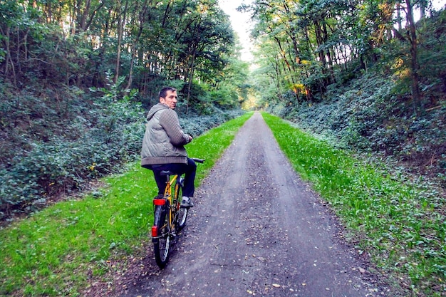 Rear view portrait of man riding bicycle on road in forest