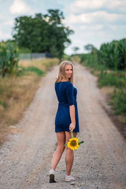 Photo rear view portrait of young woman holding sunflower while walking on dirt road