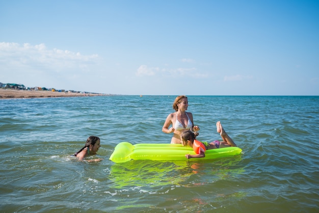 Rear view of a positive young family mom and two little daughters swim on a yellow air mattress