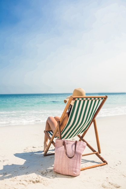 Rear view of pretty brunette relaxing on deck chair at the beach