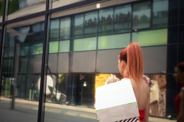 Foto vista posteriore di una donna dai capelli rossi che porta sacchetti da spesa mentre cammina per la città